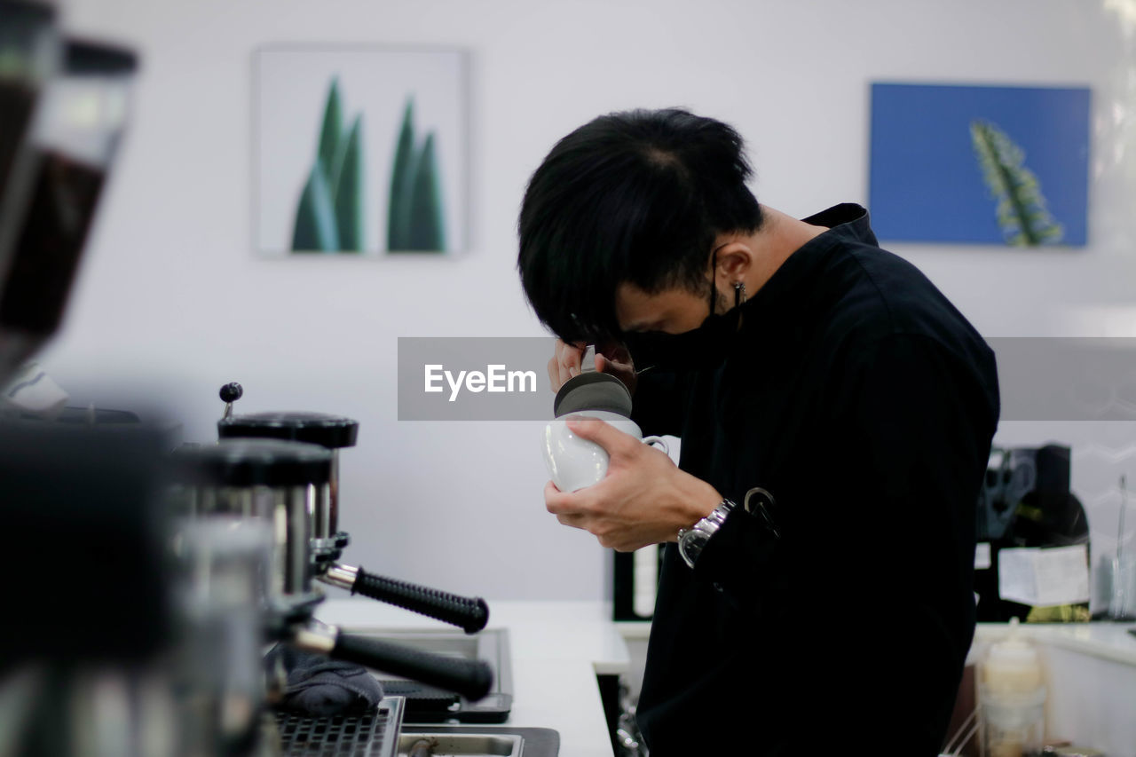 REAR VIEW OF MAN HOLDING COFFEE AT HOME