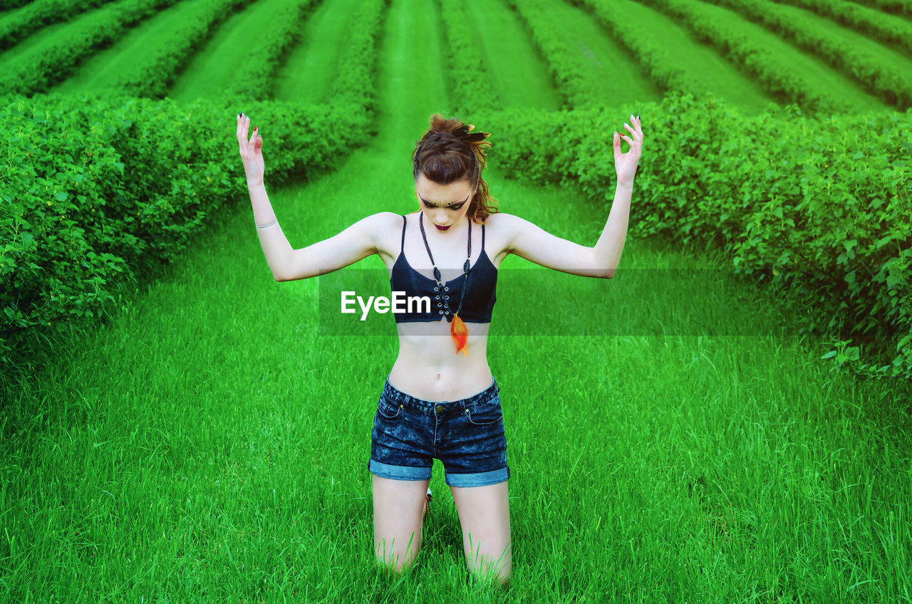 Woman with arms raised kneeling on grassy land