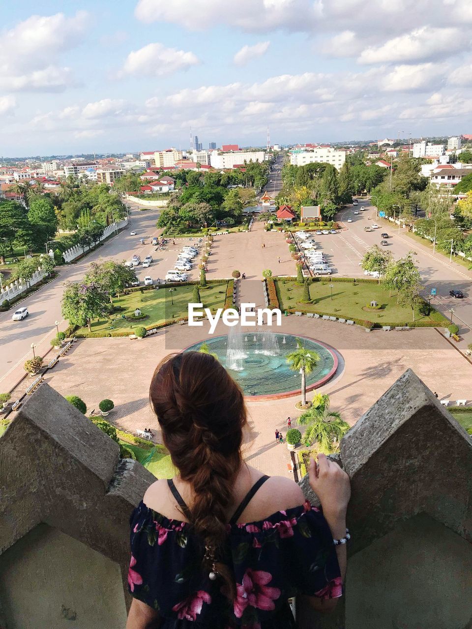 Rear view of young woman looking at view while standing by retaining wall against cloudy sky