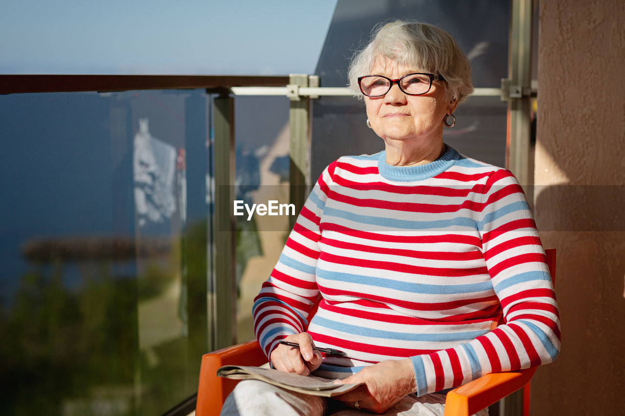 Senior woman in glasses sitting on balcony near the sea
