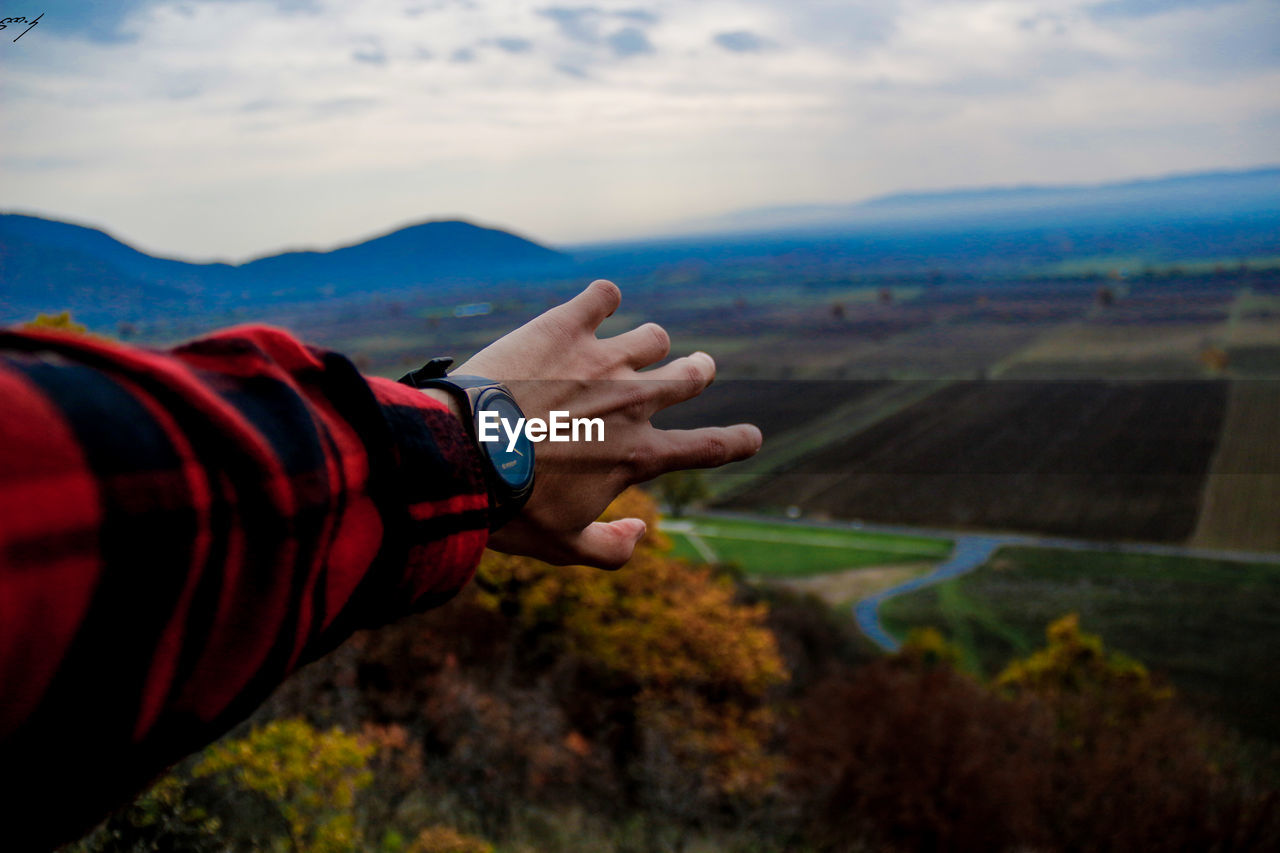 Cropped hand of man reaching landscape against sky