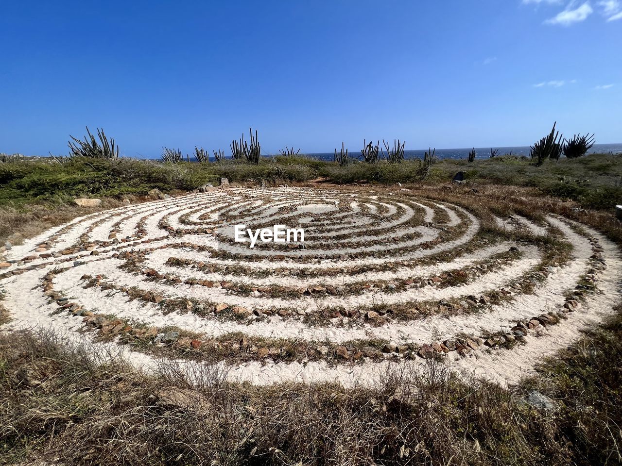 soil, field, landscape, agriculture, labyrinth, nature, sky, geometric shape, outdoor structure, land, pattern, plant, no people, circle, grass, shape, maze, sand, travel, outdoors, day, plain, environment, travel destinations, rural area, tree, history, rural scene, clear sky, concentric, blue, scenics - nature, road surface, tourism, walkway