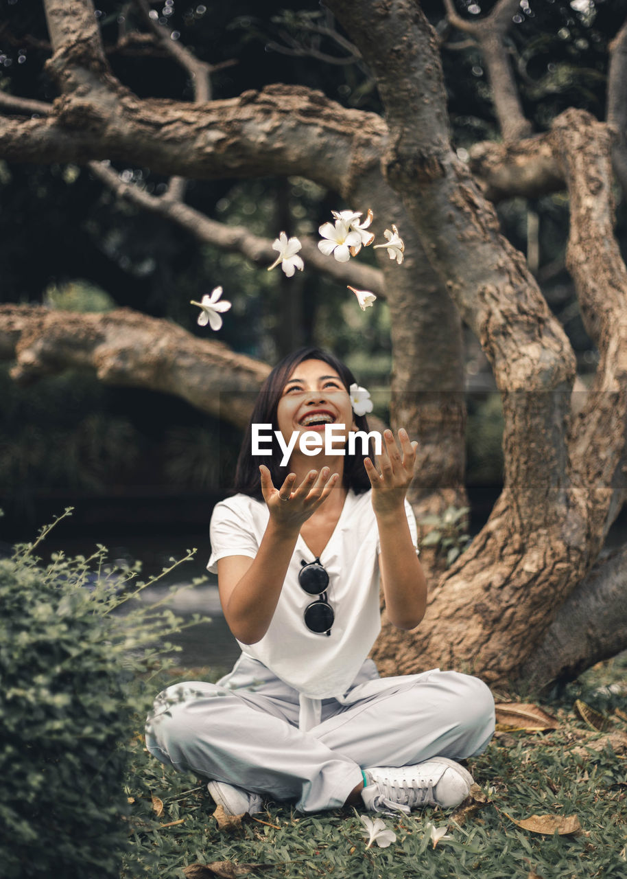 Smiling woman throwing flowers in forest