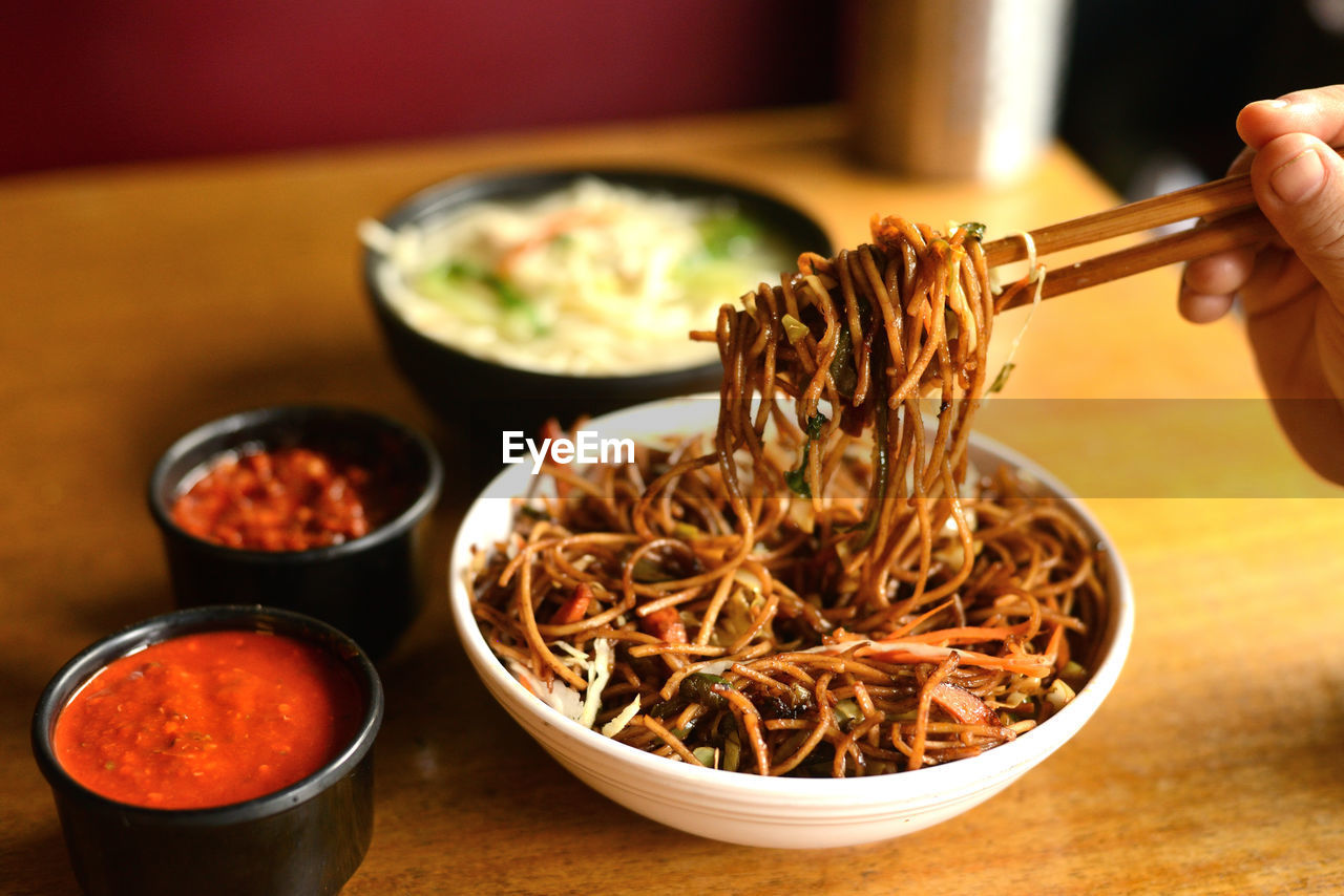 food and drink, food, hand, bowl, asian food, dish, cuisine, healthy eating, wellbeing, indoors, one person, freshness, spice, holding, close-up, focus on foreground, lifestyles, table, chinese food, kitchen utensil, adult, meal, ingredient, chopsticks, vegetable