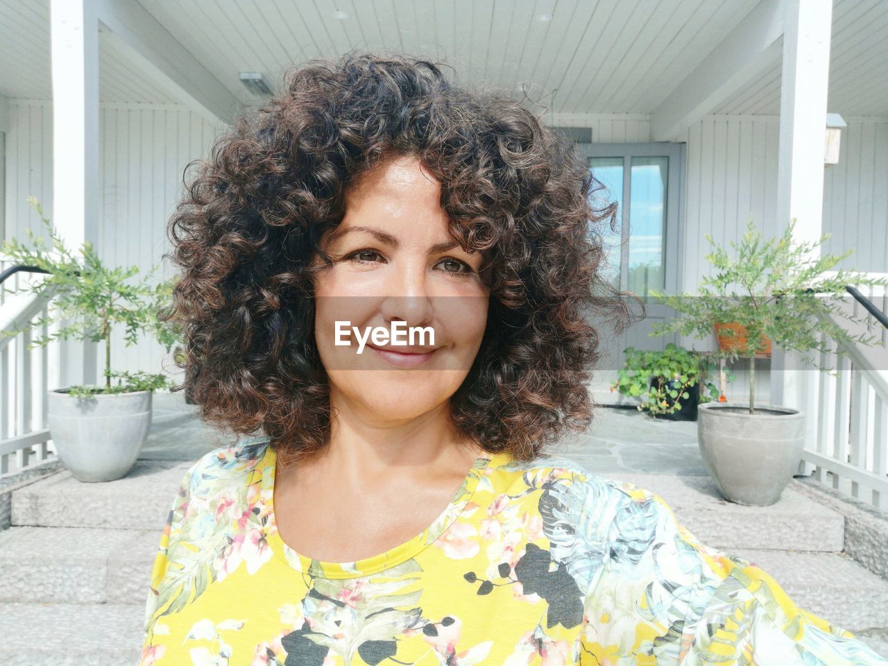 Smiling mature woman with curly hair against house