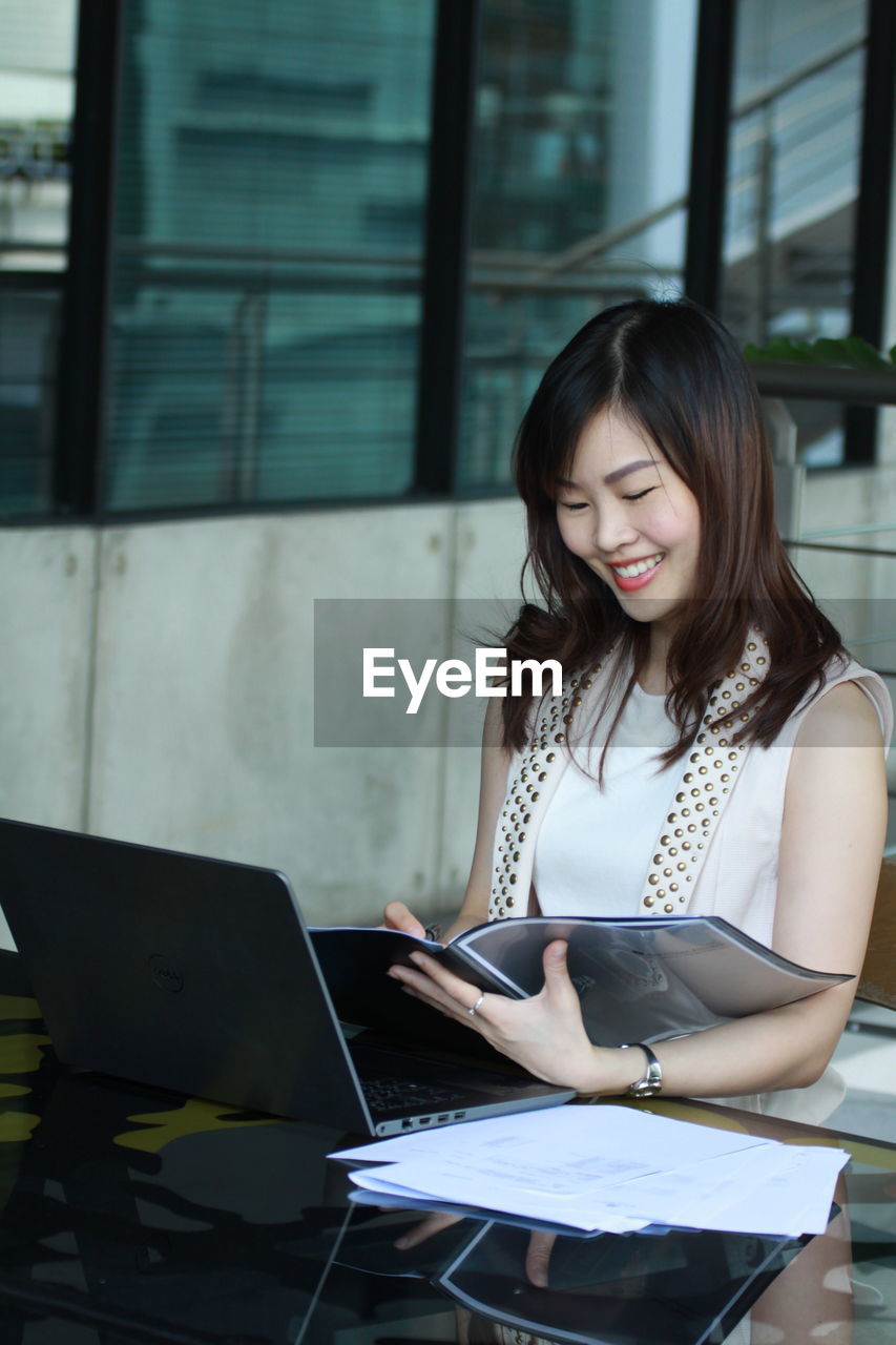 Smiling businesswoman reading file while sitting at desk