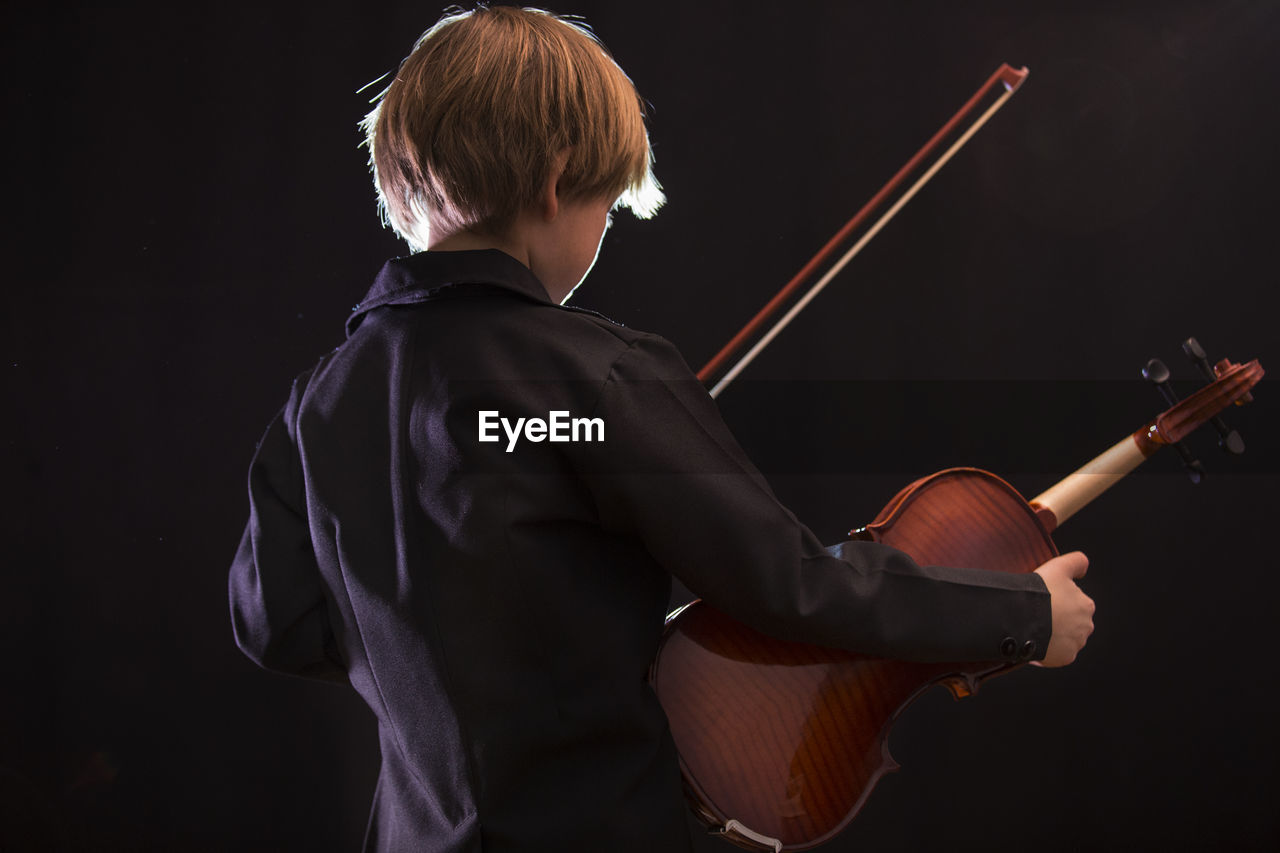 Boy playing violin against black background