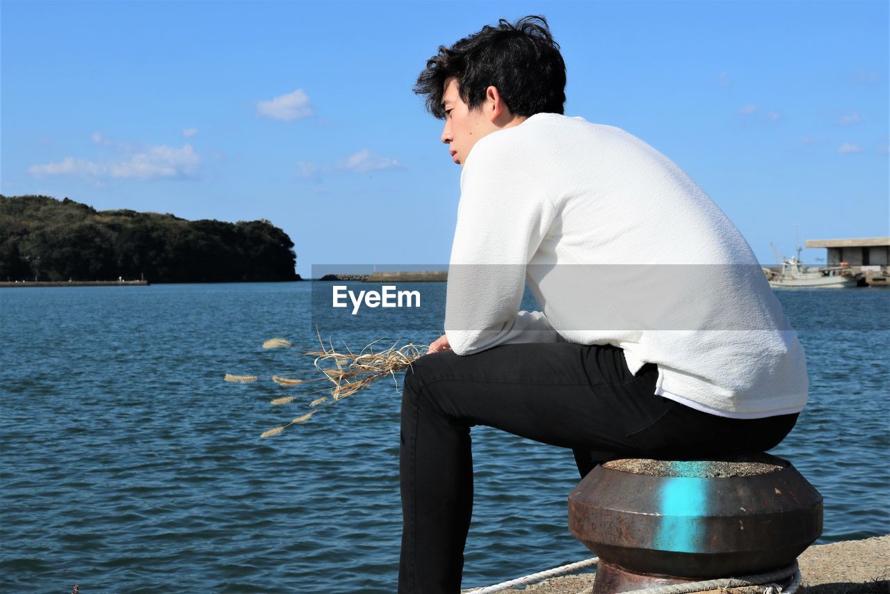 Rear view of man sitting by sea against sky