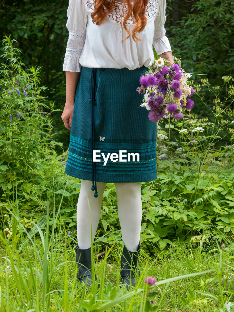 LOW SECTION OF WOMAN STANDING ON FLOWERING PLANTS