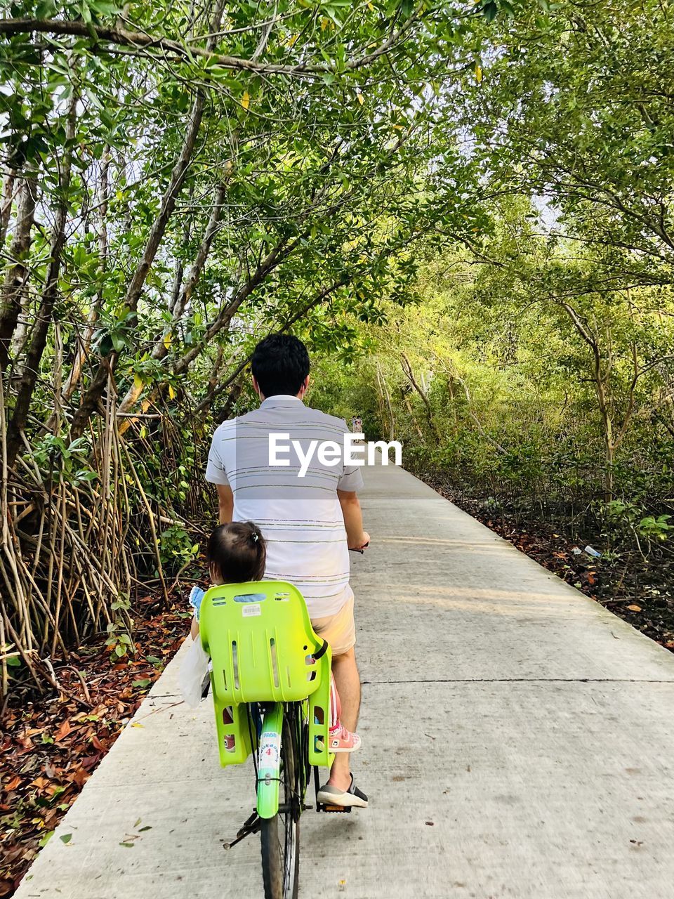 Rear view of man riding bicycle on road with his daughter