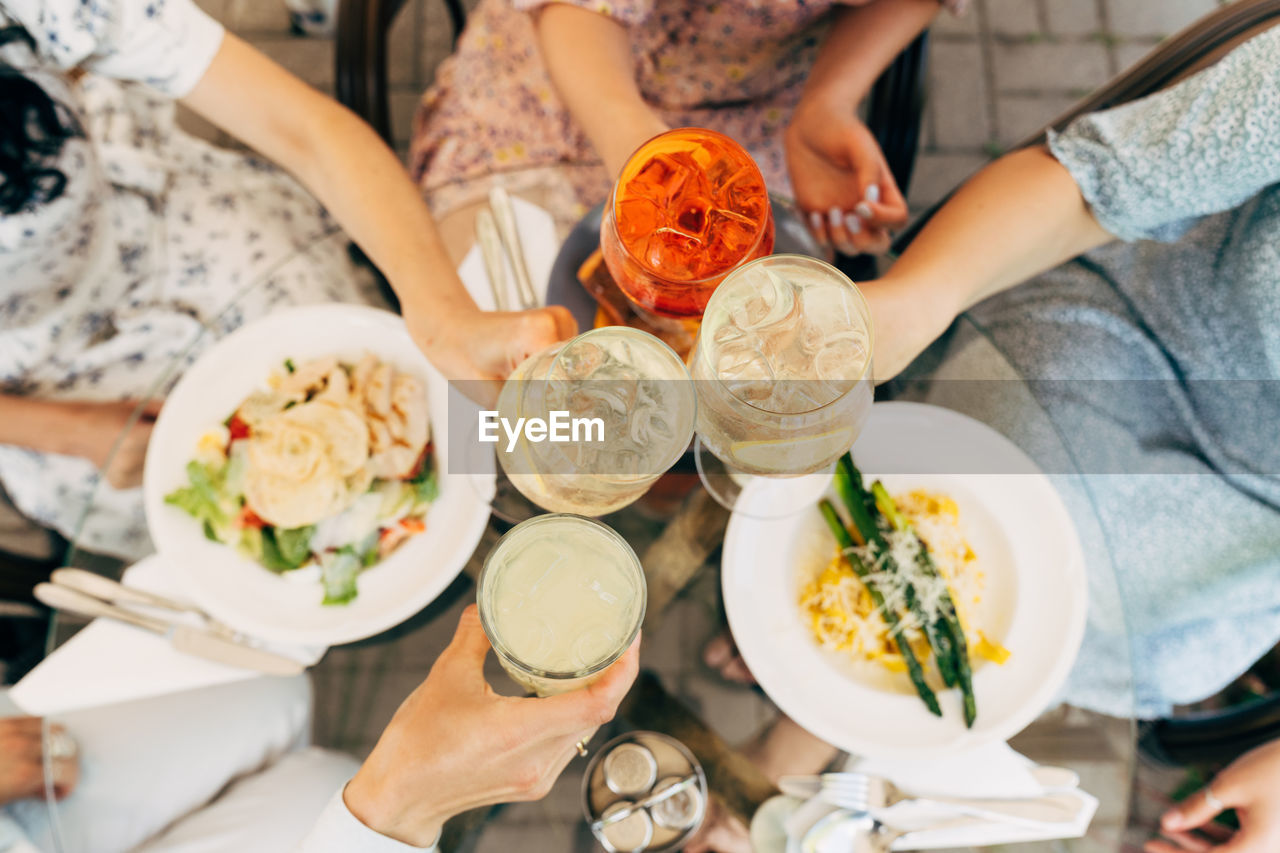 Overhead view of friends having brunch, toasting, saying cheers holding aperol spritz cocktails. 