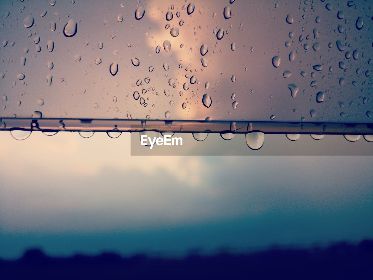 Close-up of raindrops on window against sky during rainy season