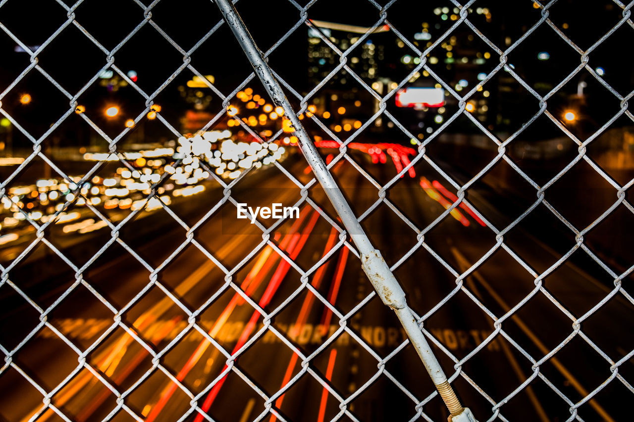 Light trails on road seen through chainlink fence