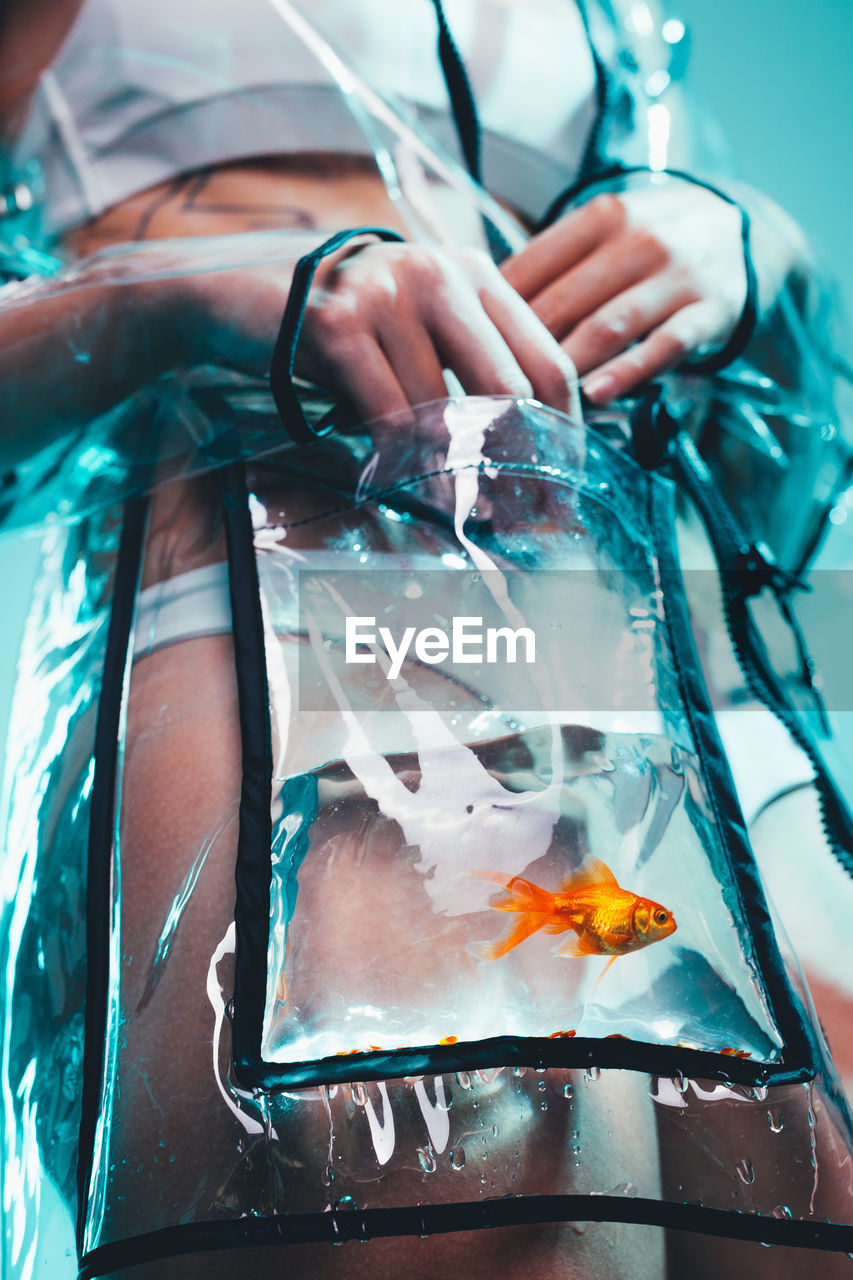 Midsection of woman with fish in transparent raincoat