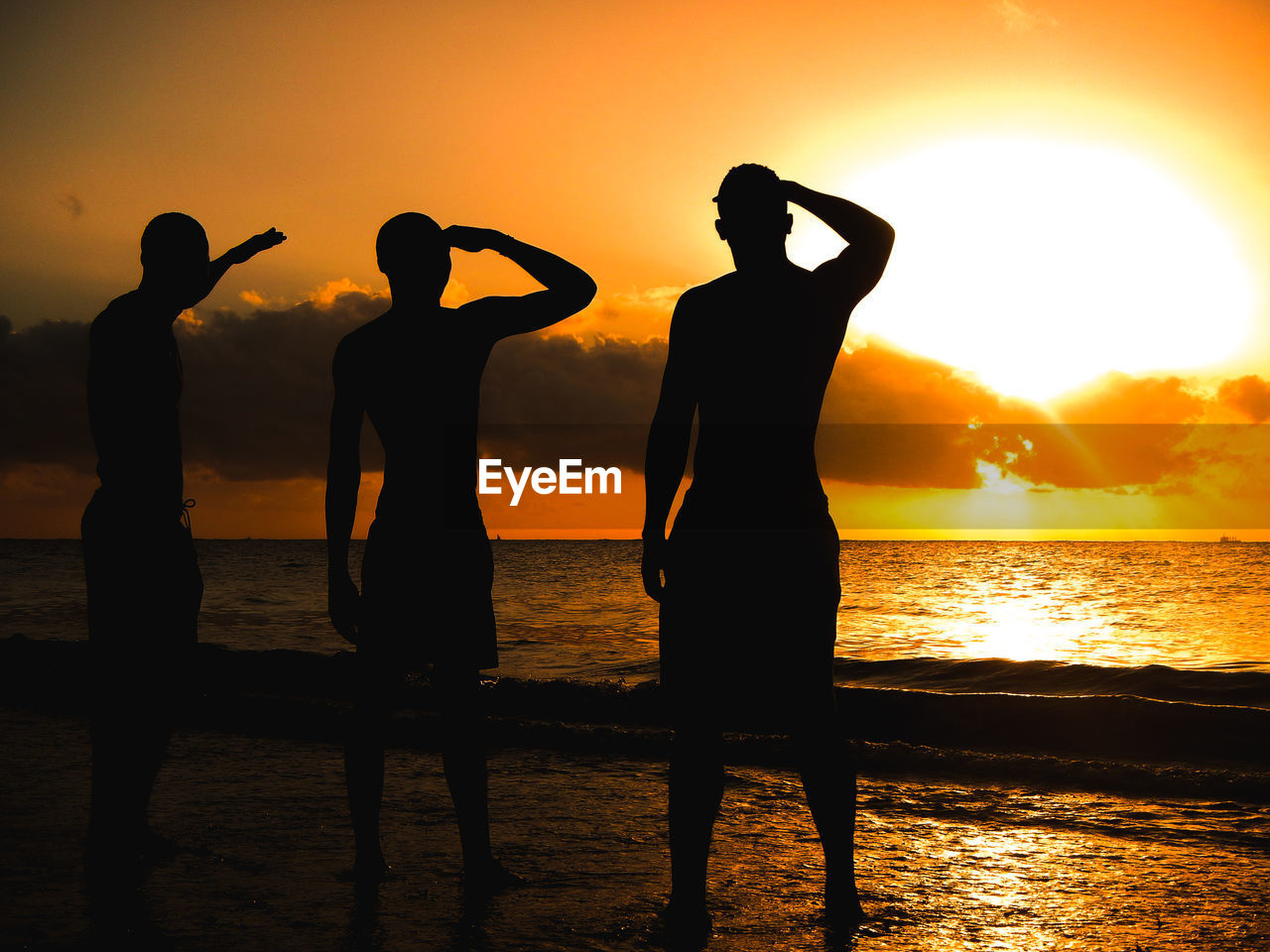 Silhouette friends standing at beach against sky during sunset