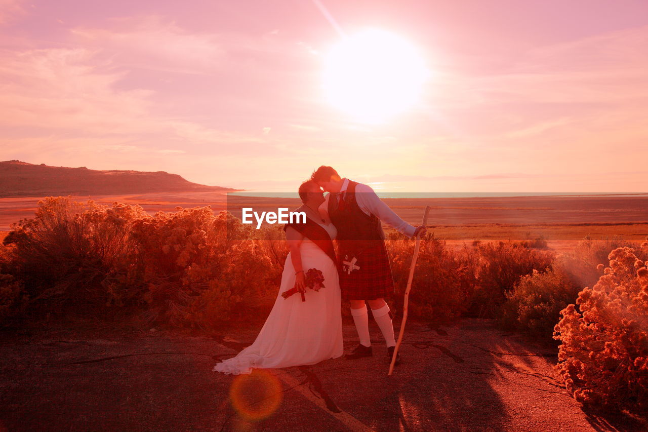 Romantic lesbians standing on field against sky on sunny day