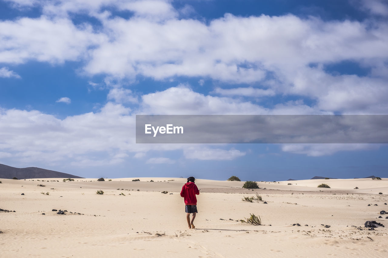 Rear view of teenage boy walking at desert against cloudy sky