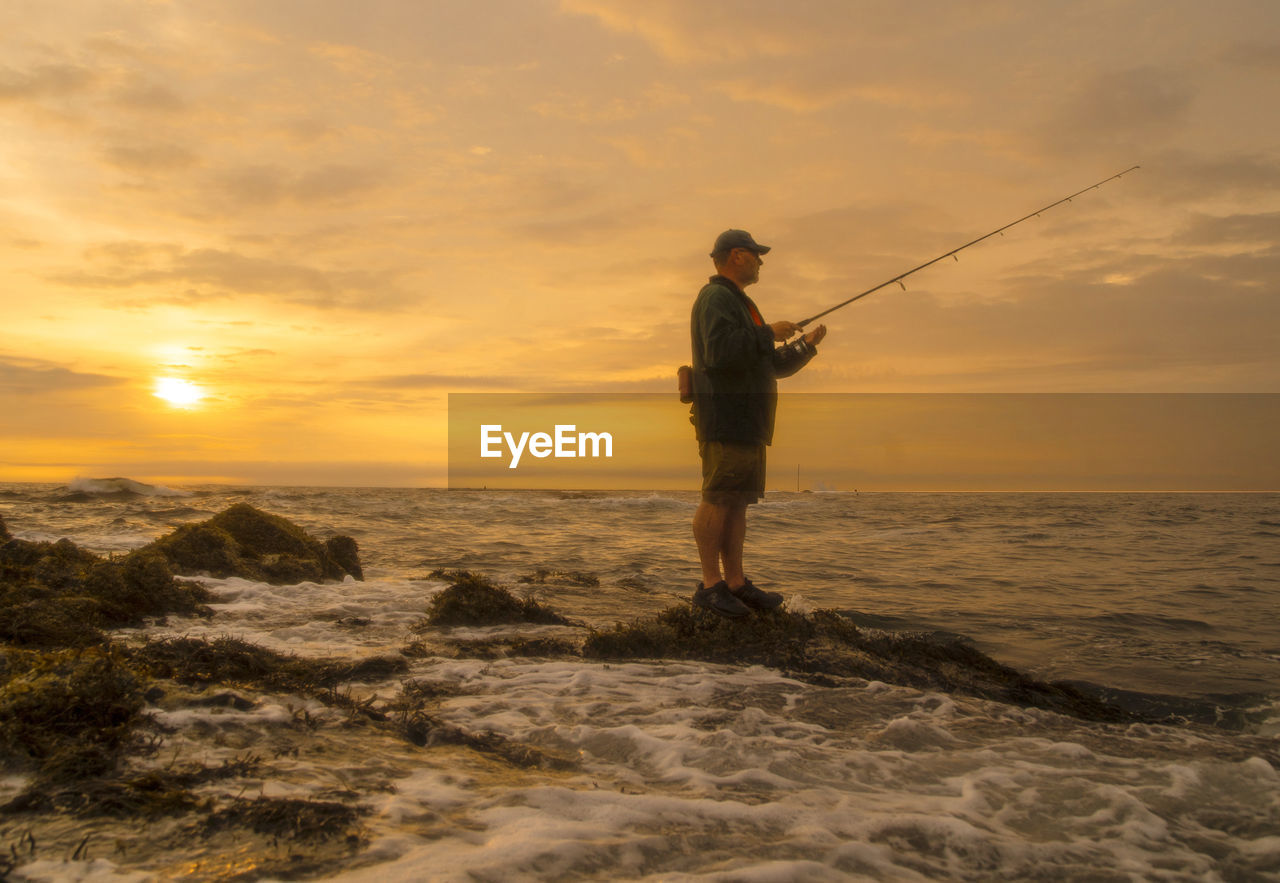 Maine coastal fisherman waits for a striped bass to bite as sun rises.