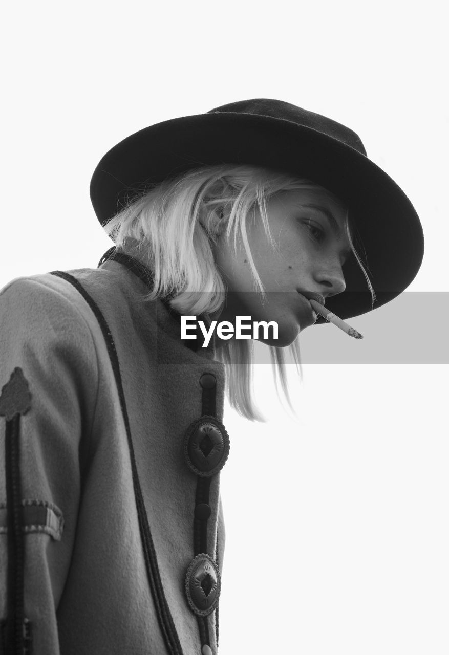 Low angle view of young woman smoking cigarette against clear sky