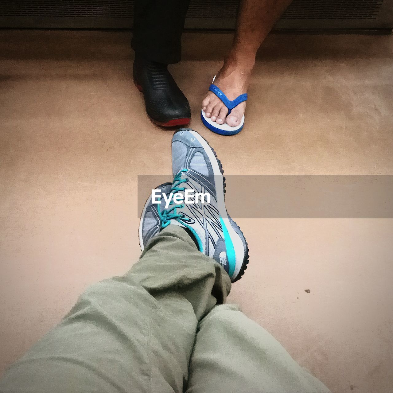 LOW SECTION OF WOMAN WEARING CANVAS SHOES ON FLOOR