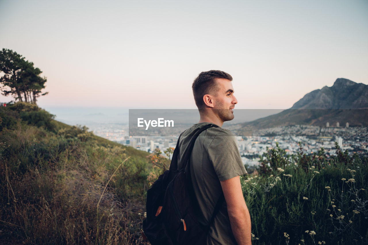 Young man standing on landscape against clear sky during sunset