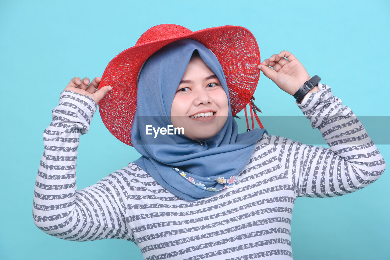 PORTRAIT OF SMILING YOUNG WOMAN WEARING HAT AGAINST CLEAR BLUE SKY