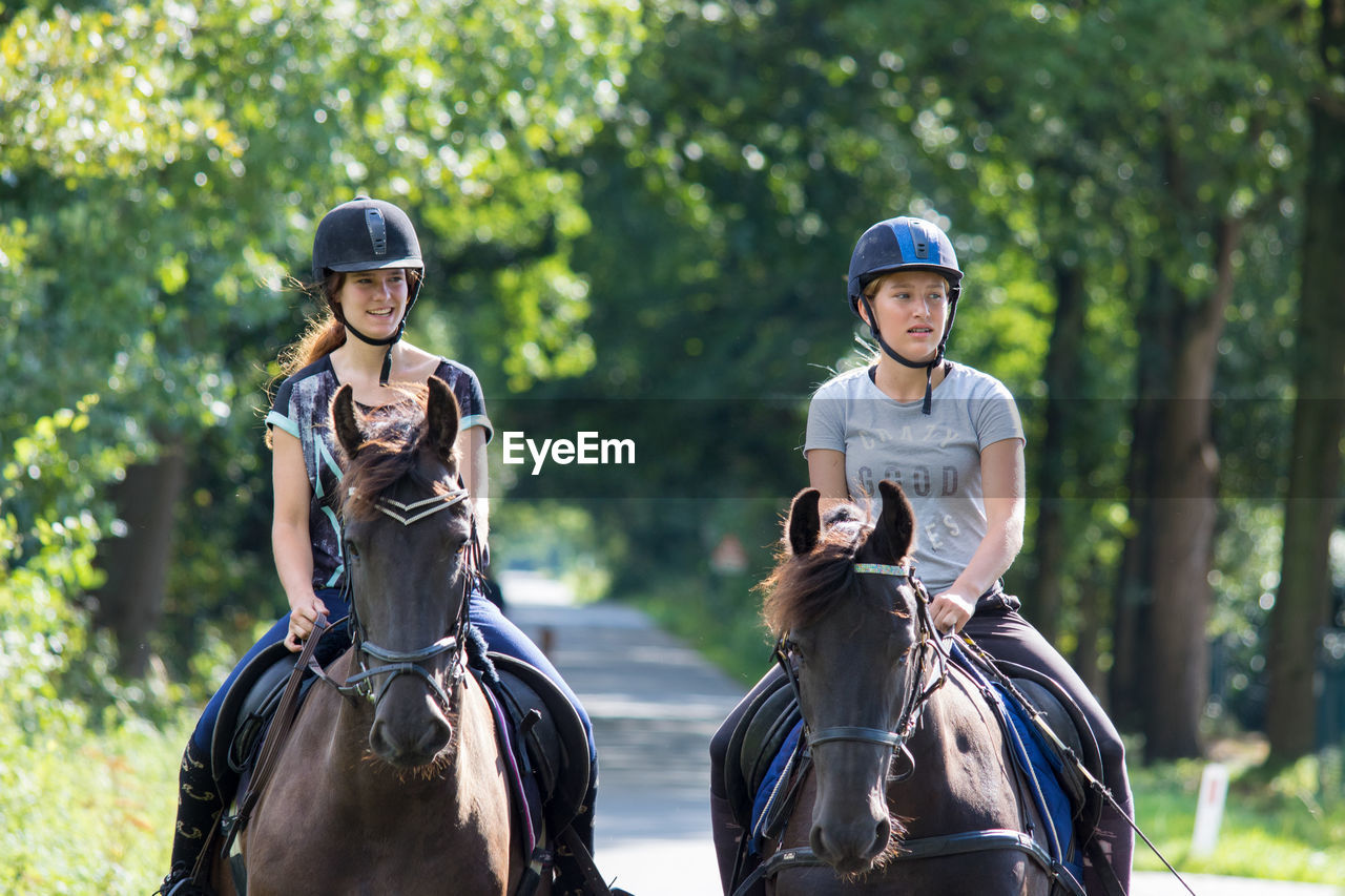 Friends looking away while riding horses at park