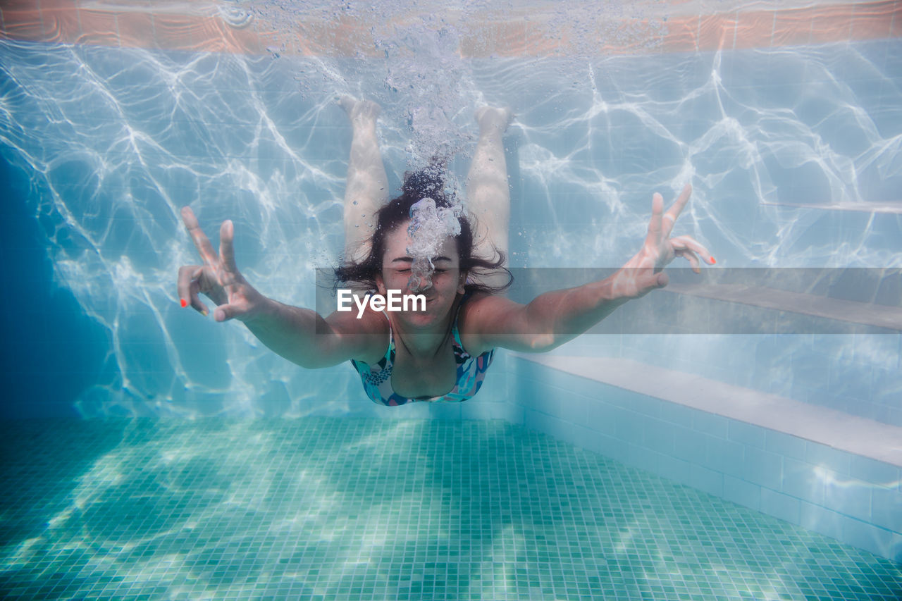 Woman gesturing while swimming underwater in pool