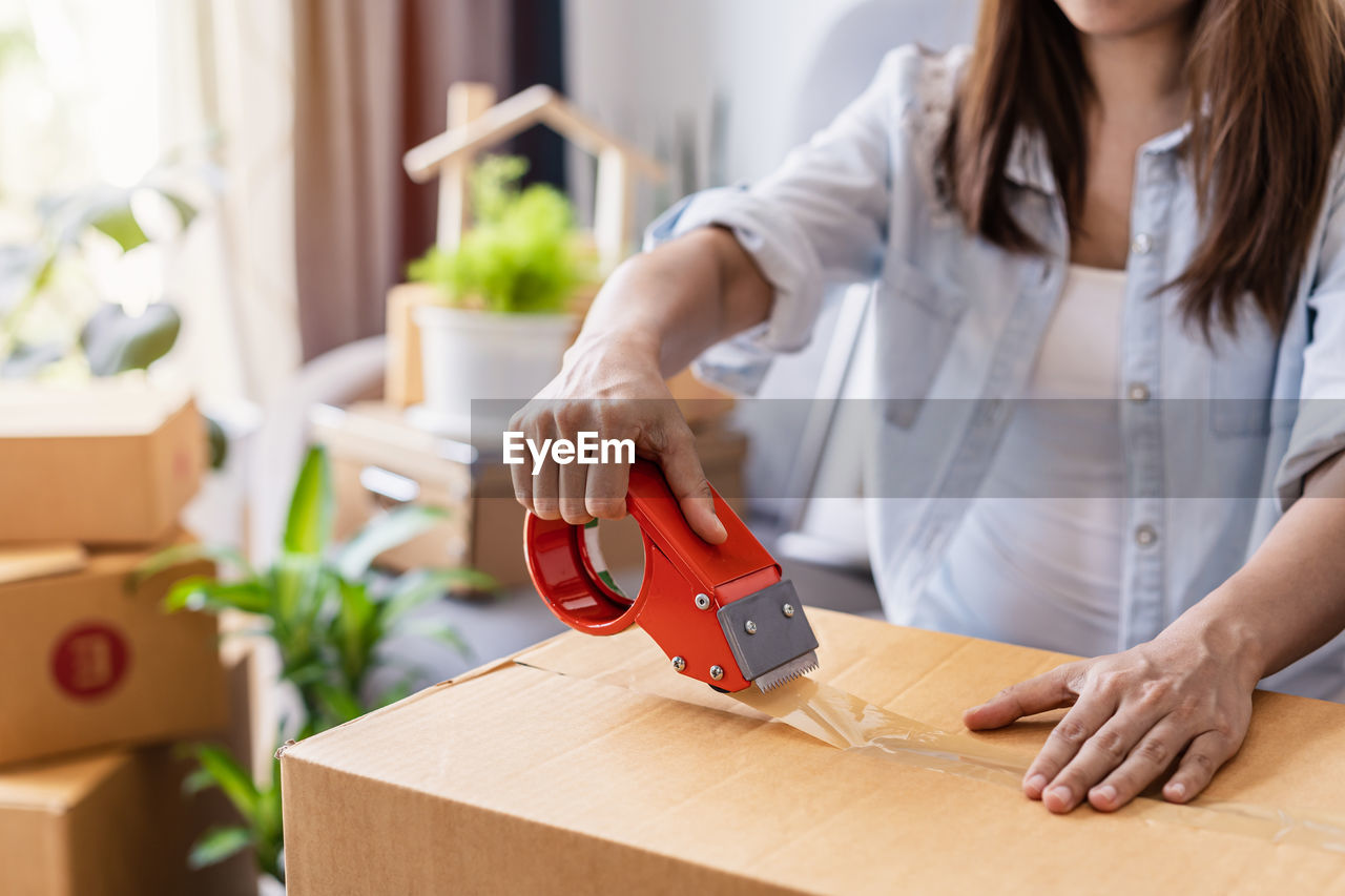 MIDSECTION OF WOMAN HOLDING CAMERA WHILE STANDING ON BOX