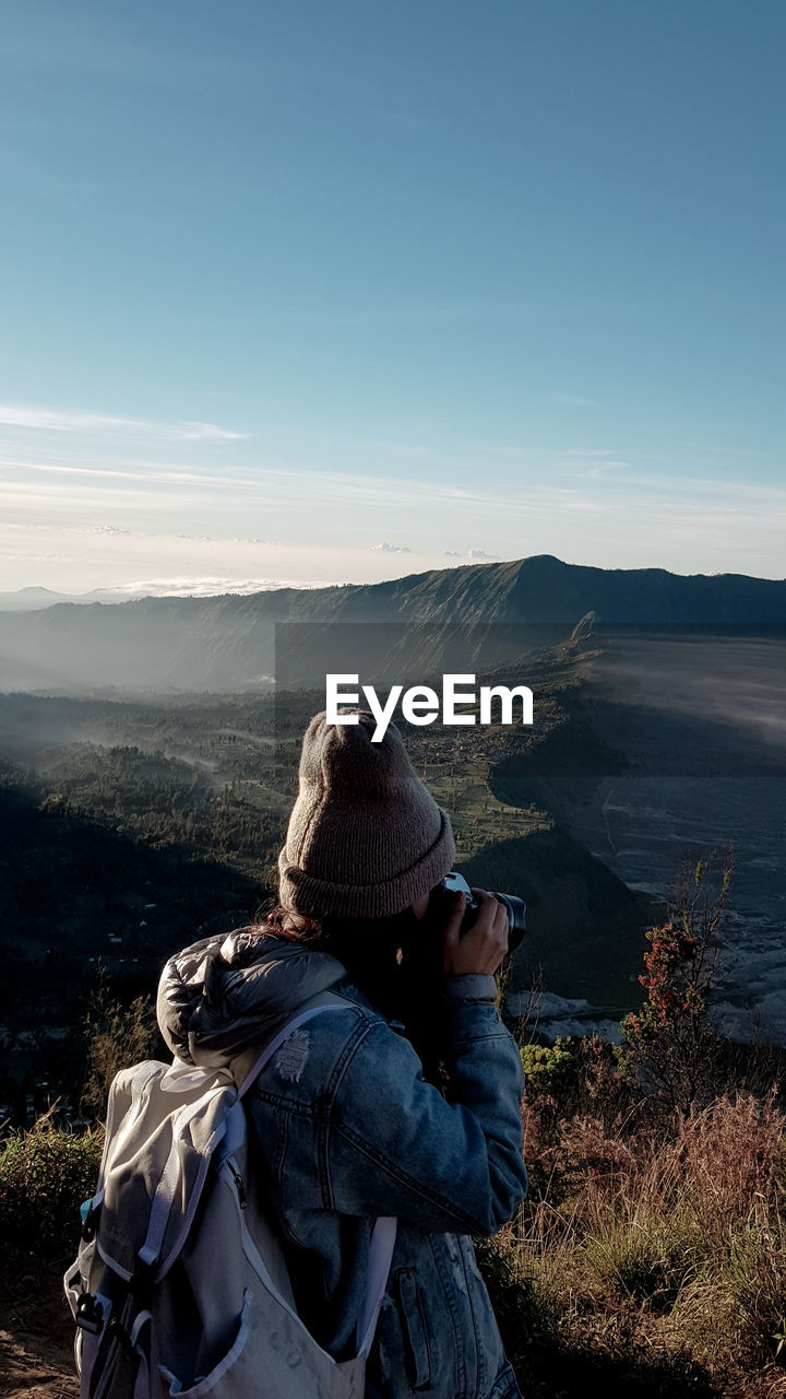 Side view of woman photographing on mountain against sky