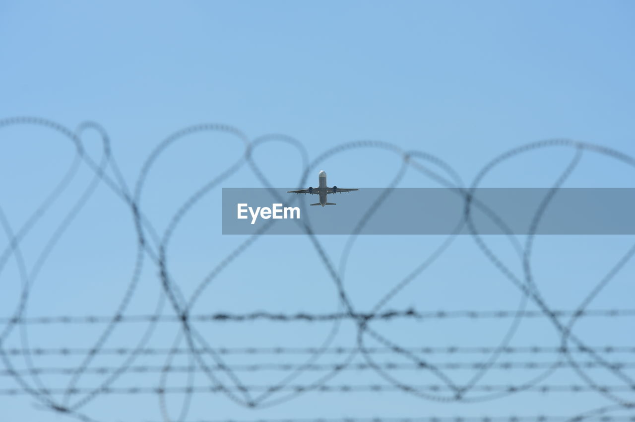 Close-up of barbed wire against sky seen through fence