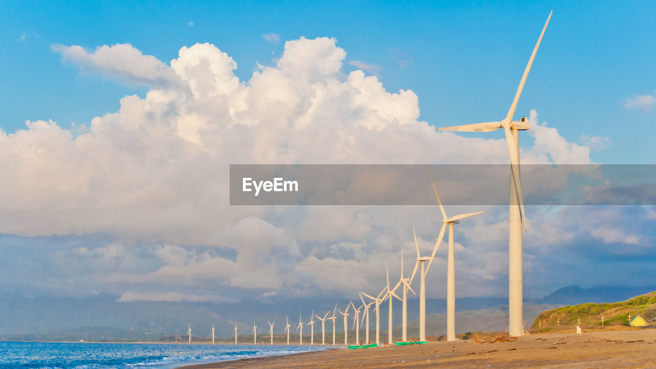 Wind turbines on beach against cloudy sky