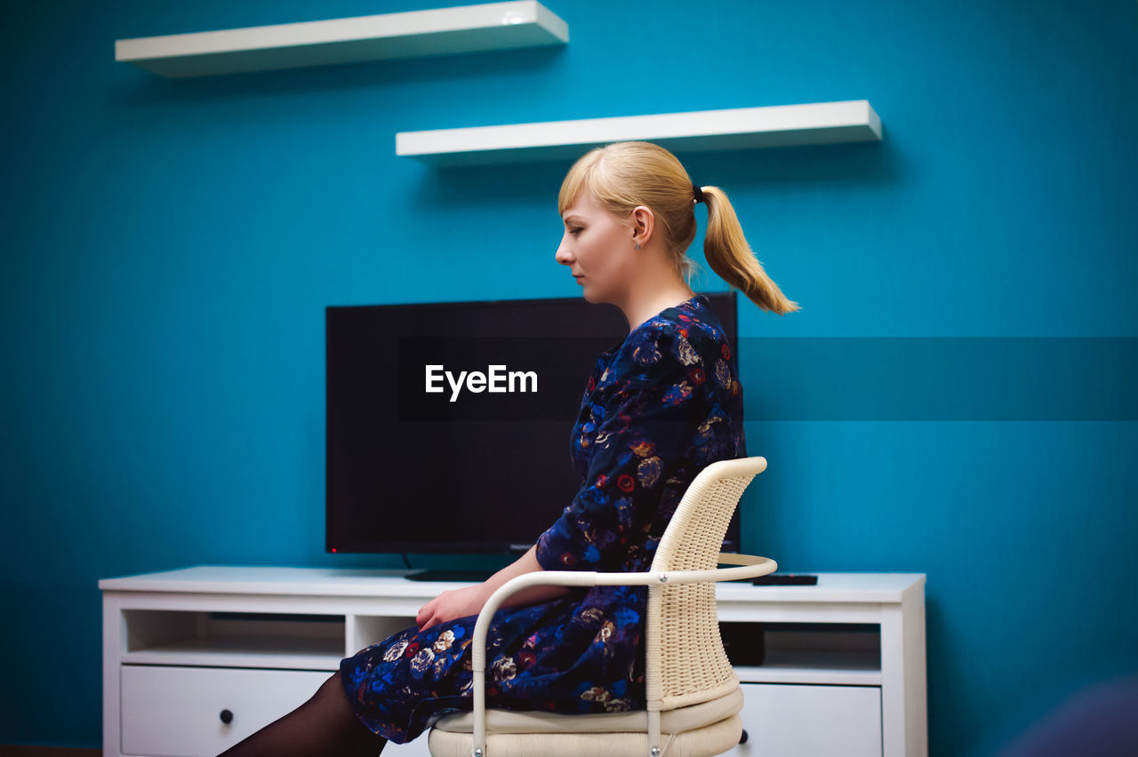 Side view of young woman sitting on chair at home