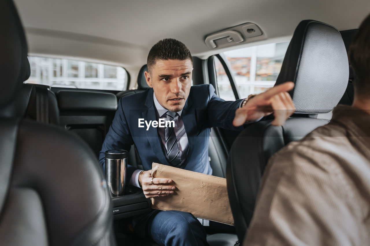 Businessman assisting driver while sitting in taxi