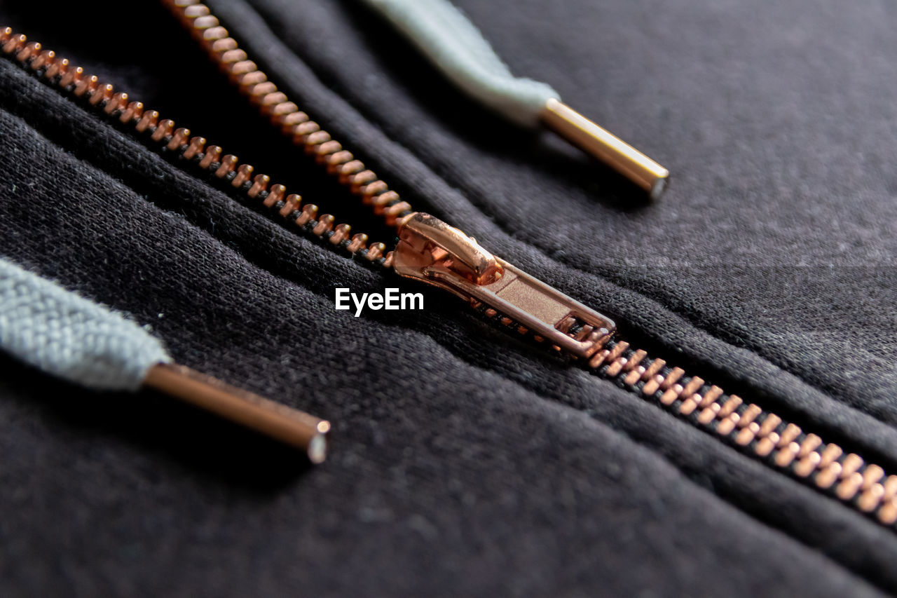 Copper colored fashion zipper macro view showing black sweatshirt with partial opened metal zipper