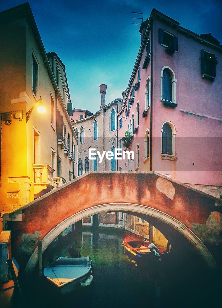 BRIDGE OVER CANAL AMIDST BUILDINGS IN CITY