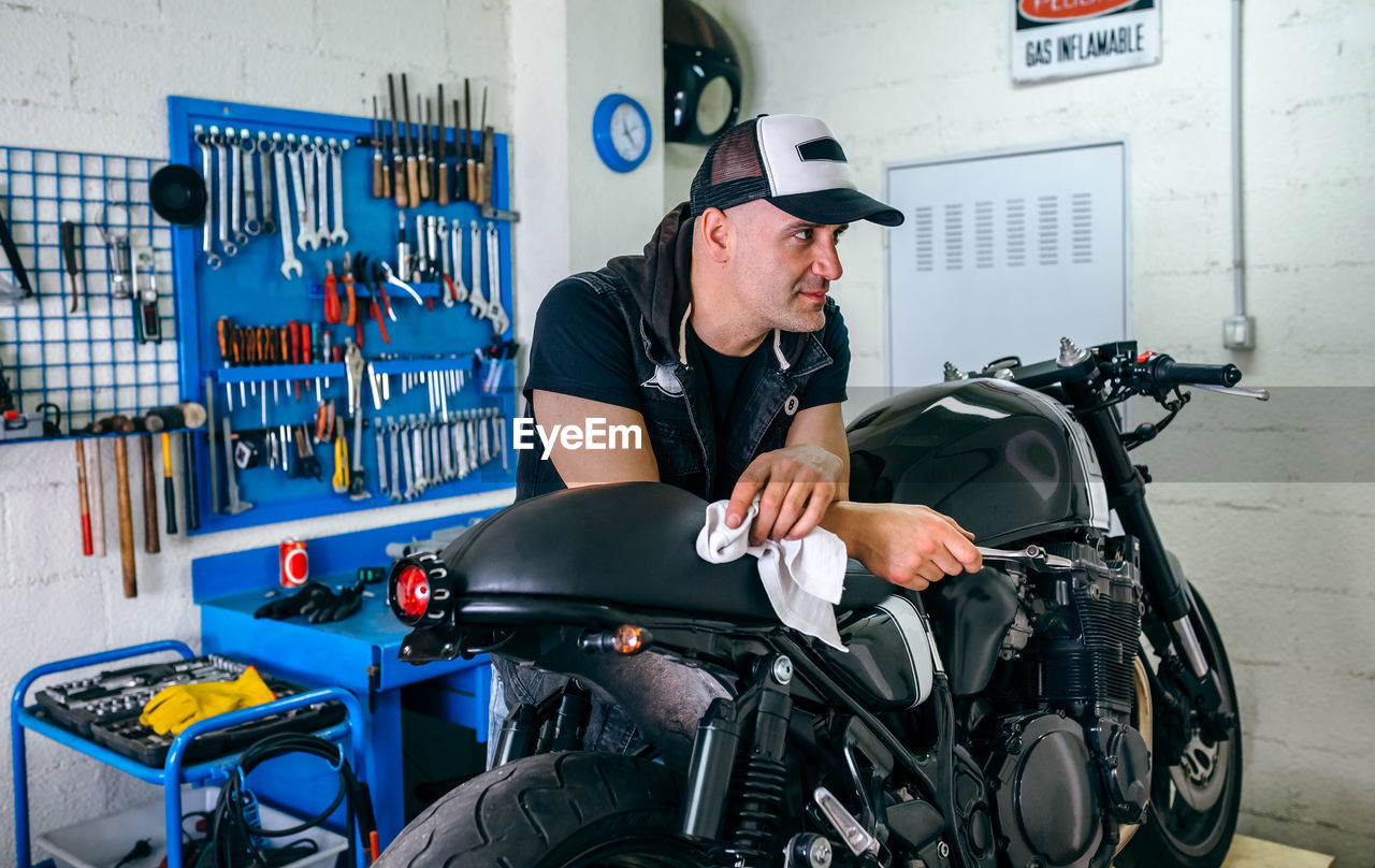 Man holding tool while leaning on motorcycle in garage