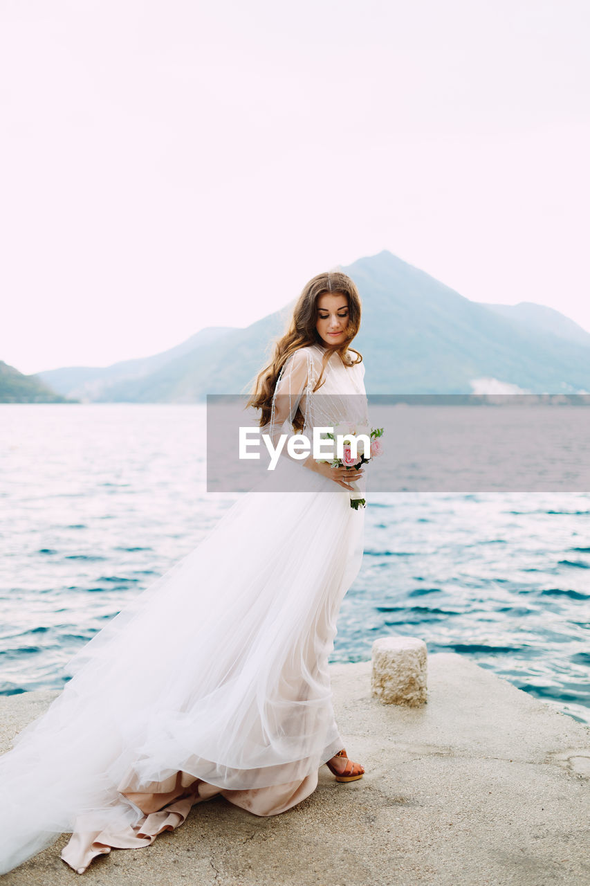 Woman standing on wall by sea against sky