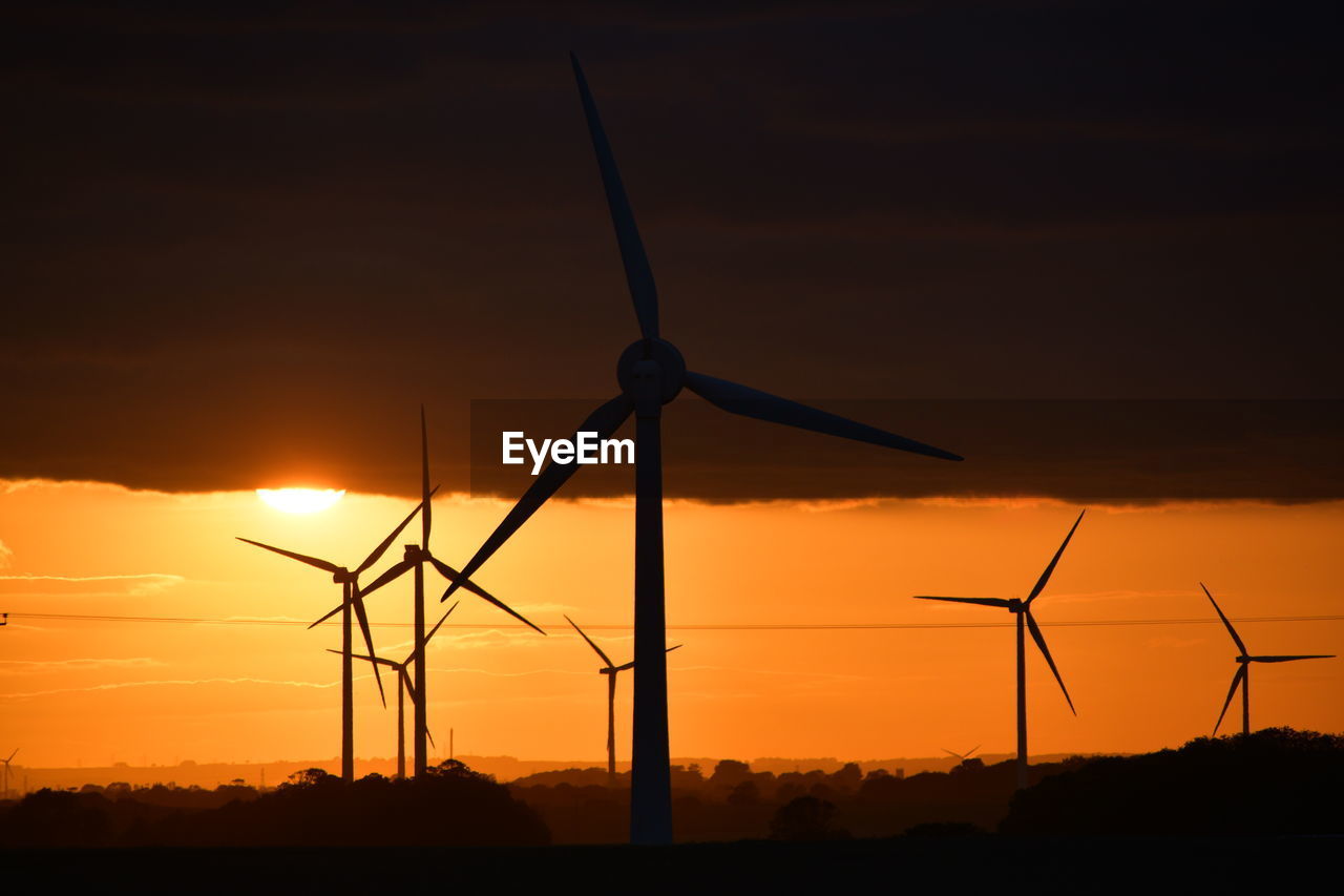 A bright red sunset through wind turbines