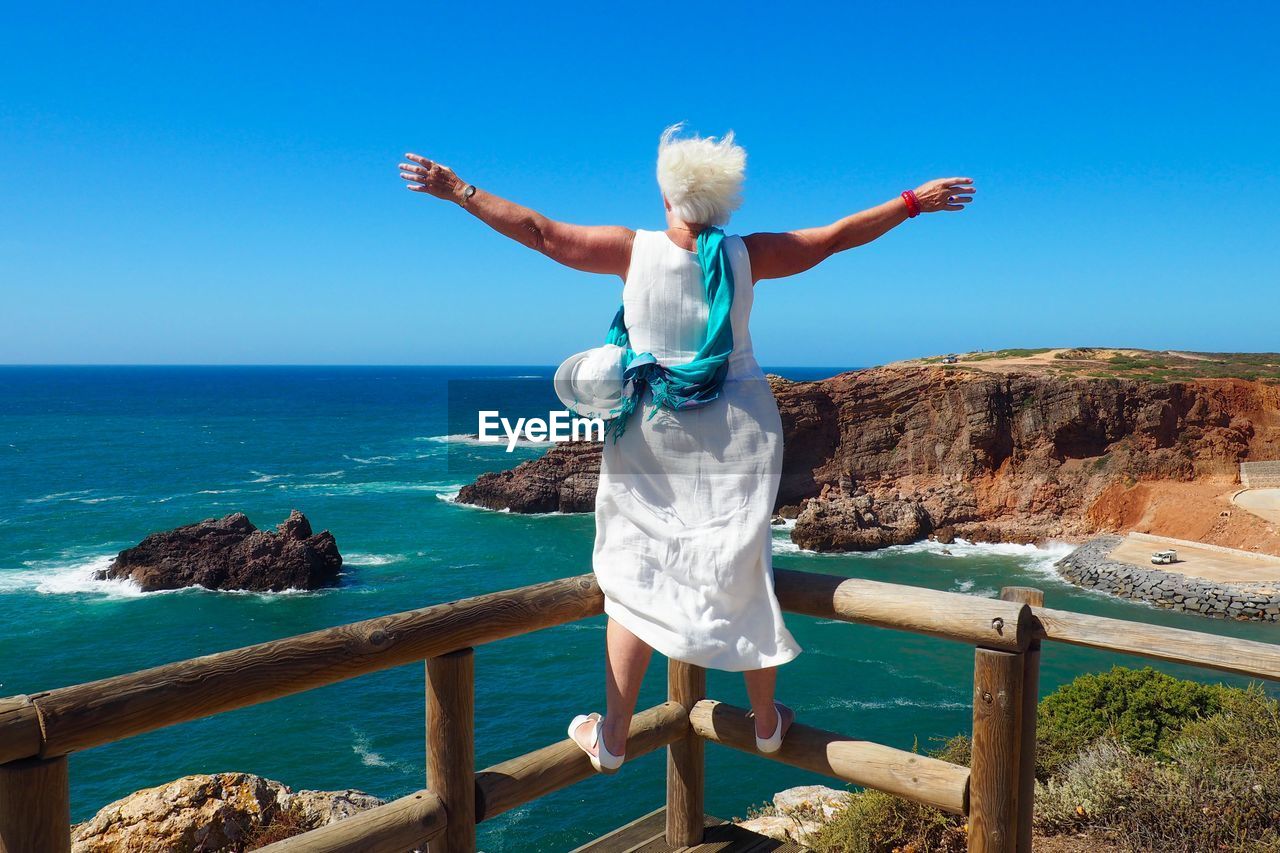 Rear view full length of woman with arms outstretched on railing against sea