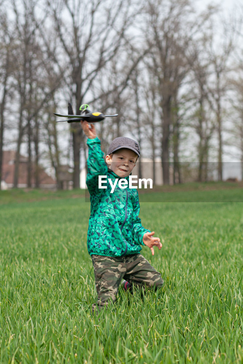 Portrait of boy holding model airplane while standing amidst plants