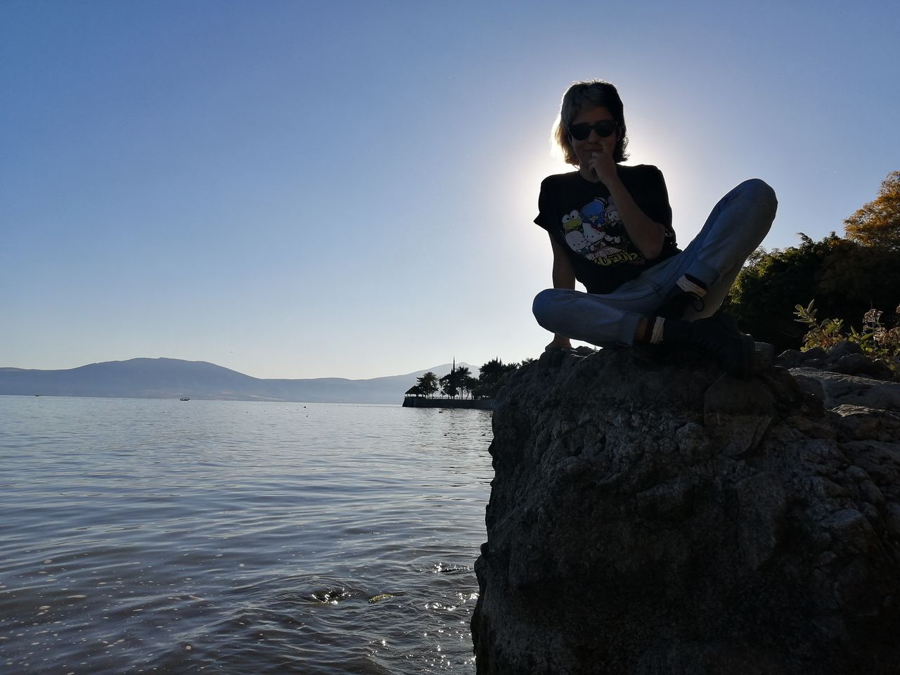 MAN SITTING ON ROCK AGAINST SEA