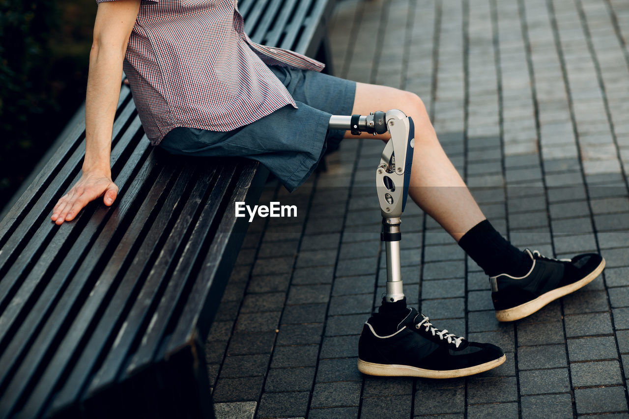 Low section of man with prosthetic equipment sitting on bench