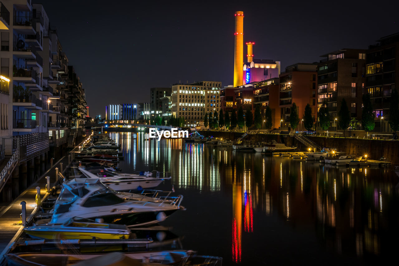 Boats moored in illuminated city against sky at night