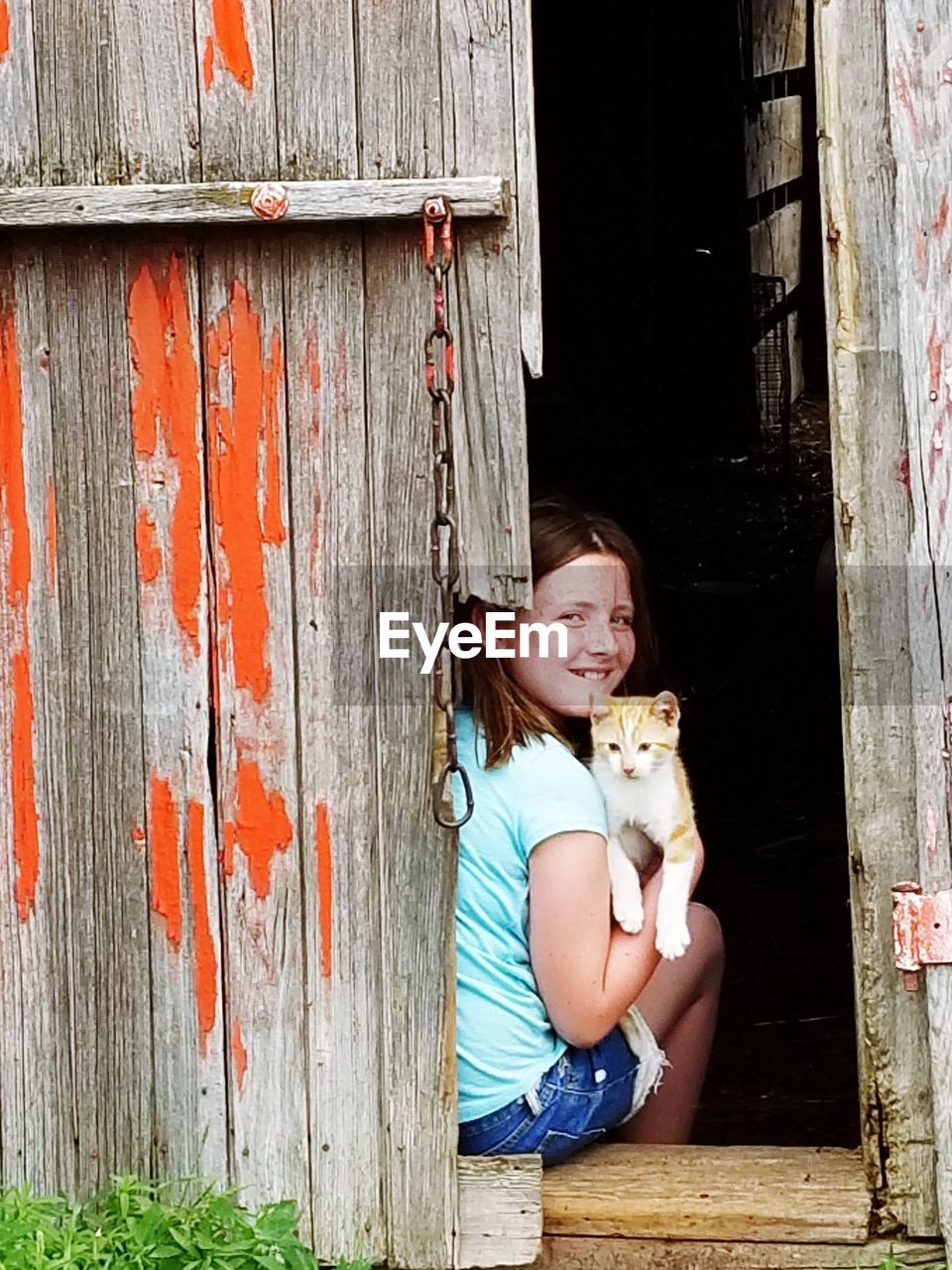 Portrait of girl holding cat while sitting at entrance