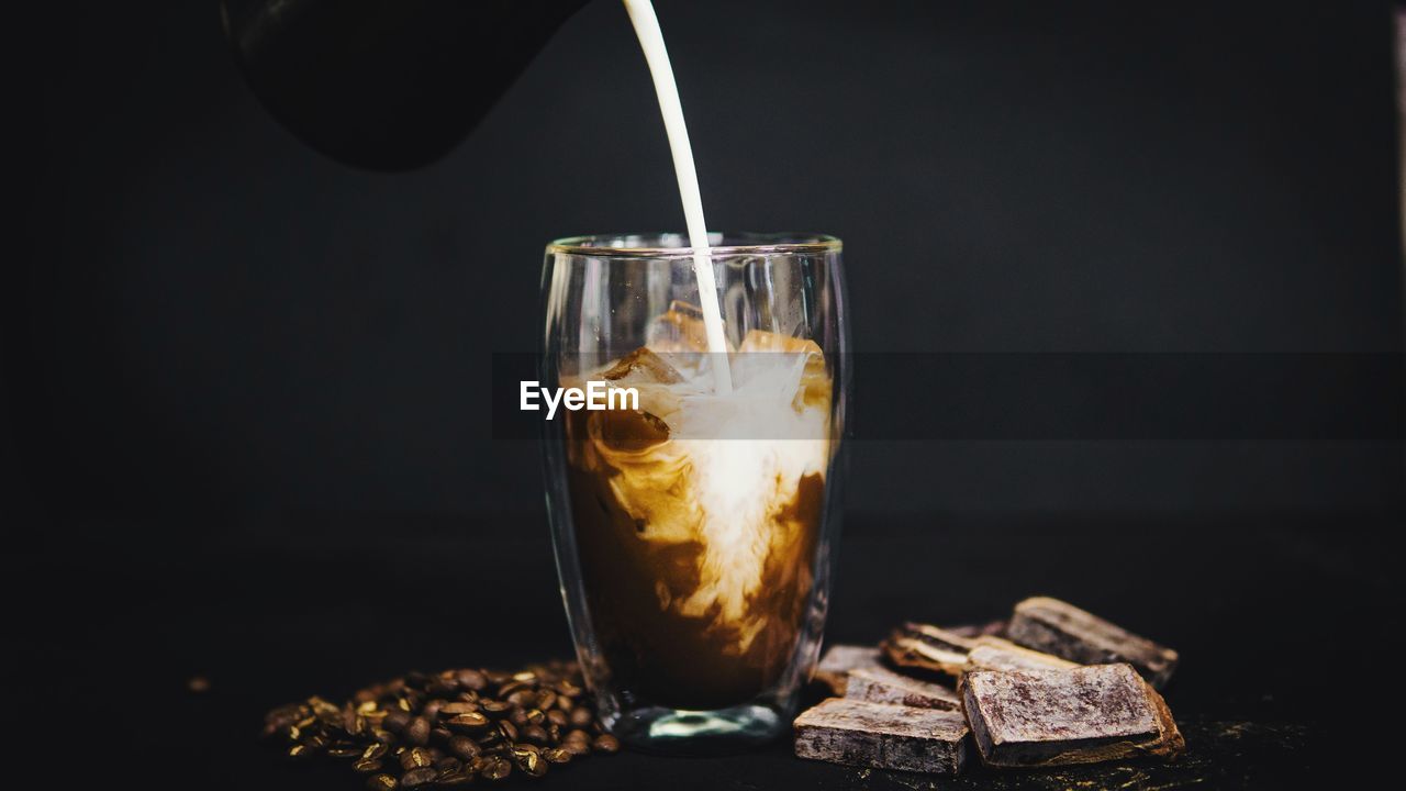 Close-up of milk pouring in iced coffee against black background