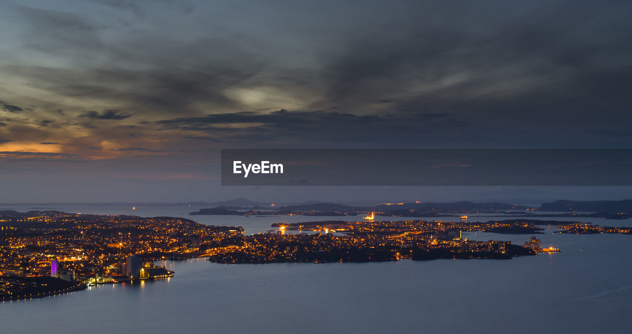 Aerial view of illuminated cityscape by sea against sky during sunset