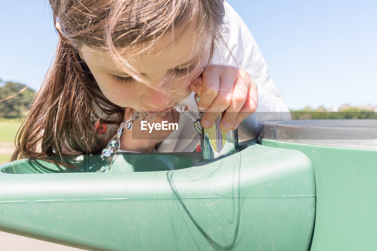 Close-up of girl drinking water from fountain in park during sunny day