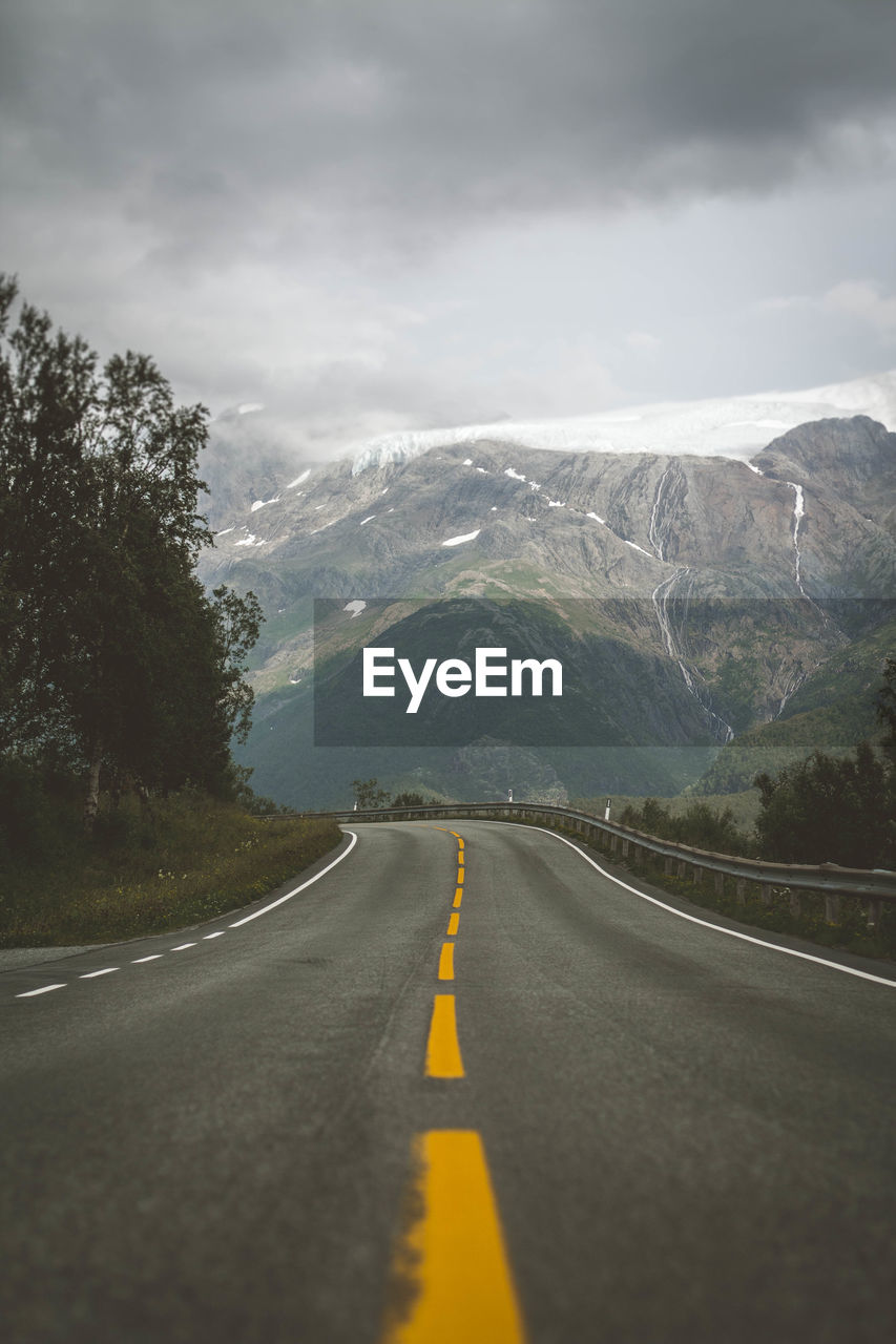 Road leading towards mountains against cloudy sky