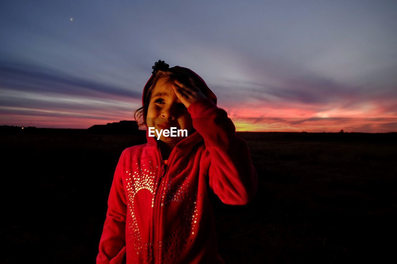 Girl crying while standing at park against sky during sunset